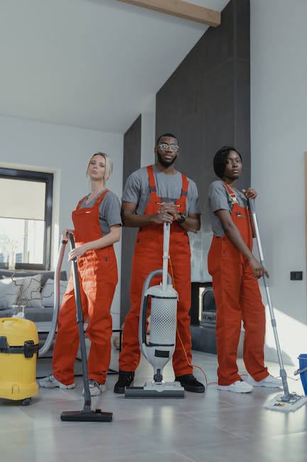A professional cleaner from Yiewsley Carpet Cleaners, dressed in a black uniform, is performing surface cleaning in a home or office setting. She is using a cloth and spray bottle on a wooden table or